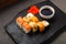 Assorted salmon and shrimp rolls on a black board next to soy sauce and ginger on a dark background.