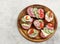 Assorted sandwiches with vegetables and sausages on the round wooden cutting board on a light gray background