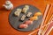 Assorted sushi on a circular black slate plate and sauce boat with soy sauce. Salmon makis, tuna and salmon nigiri, uramaki with