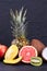Assorted tropical fruits on black textured background.