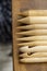 Assorted wooden knitting needles lie on a wooden table, in the background a blurred gray plaid merino wool