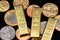 An assortment of Brazilian coins on a black reflective background with three one ounce gold ingots