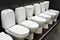 An assortment of ceramic toilets in a plumbing store. A large selection of products for a bathroom in a shopping center showcase.