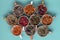 Assortment of dried relaxing tea herbs in colourful cups on blue background close up.