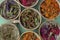 Assortment of dried relaxing tea herbs in colourful cups on mint green background.