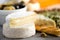 Assortment of hard, semi-soft and soft cheeses with olives, grissini bread sticks, capers, grape, on grey concrete