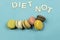 Assortment of multi-coloured macaroons on a blue background with the words diet not