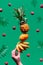 Assortment of tropical fruits, pyramid balancing o human hand on green background. Pineapple, kiwano, kiwi , lichee and banana -