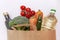 An assortment of vegetables and other foods purchased at a supermarket in a recyclable brown paper bag on a white background