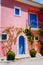 Assos village. Traditional pink colored greek house with bright blue door and windows. Fucsie plant flowers arount