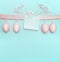 Aster greeting card with pastel pink eggs hanging on ribbon on light blue turquoise background.