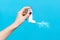 Asthma. A woman`s hand presses the pump of the inhaler, spraying the medicine. Side view. Blue background. Copy space