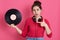 Astonish young charming girl holding music plate in hand and pointing at it with forefinger, keeps mouth opened, sees vintage disc