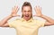 Astonished blonde woman gestures with both hands, screaming loudly, wearing yellow t-shirt, posing against white studio background