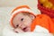 Astonished cute newborn baby dressed in a knitted orange costume