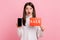 Astonished female standing with open mouth, holding sale card and cell phone with empty display.