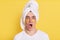 Astonished man wrapped towel on head doing morning cosmetology procedures, posing with patches under eyes isolated over yellow