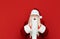 Astonished Santa Claus stands against a red wall and looks into the camera. Portrait of shocked man in santa costume isolated.