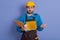 Astonished shocked young builder in yellow helmet standing with mouth opened and being very surprised, holding yellow paper folder