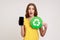Astonished teen girl in yellow casual T-shirt showing mobile phone with blank screen and recycling symbol, being shocked, keeps