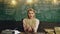 Astonished woman reads a book at classroom against background of green chalkboard. Shocked female student holds the book