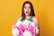 Astonished woman with widely opened mouth holding white and pink peonies, being shocked, standing against yellow background,