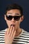 Astonished young Asian man in sunglasses covering his mouth by p