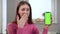 Astonished young beautiful woman looking at camera with excited facial expression looking at green screen app on