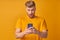 Astonished young caucasian man joyfully looks at smartphone on yellow background