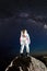 Astronaut standing on rocky mountain under starry sky.