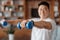 Athlete asian man doing hands exercise with dumbbells in living room interior, doing strength workout at home