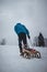 Athlete in blue winter clothes pulls to the top of the slope a wooden sled with accessories for photography and a plastic