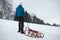 Athlete in blue winter clothes pulls to the top of the slope a wooden sled with accessories for photography and a plastic