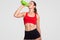 Athlete female drinks water, being thirsty after jogging during sunny day, has slim body, dressed in casual top and shorts, poses