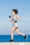 Athlete girl in gray top and shorts running alonge seafront