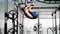 The athlete hangs on the horizontal bar and raises his legs up. Side view