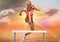 Athlete jumping over hurdles against sky in background