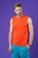 Athlete on violet background. Muscular man in orange vest and blue shorts, sportswear fashion. Fit and confident. Sport