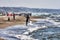 Athlete walks among the foam of the waves shore with his kite surfing board at Roman beach crowded by bathers and people