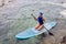 athlete woman in blue swimsuit and bandana on sit paddle board on quiet blue ocean. Sup surfing in water