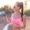 Athlete woman listening music looking at smartphone after workout in nature outdoors portrait summer evening on the