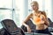 Athletic blond woman with bottle of water on treadmill in gym.