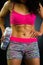 Athletic brunette woman wearing pink top and matching shorts, holding water bottle posing for camera revealing very fit upper body