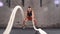 Athletic female actively in a gym exercises with battle ropes during her cross fitness workout. slow motion