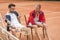 athletic friends with wooden rackets sitting on chairs after training