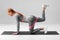 Athletic girl doing kickback exercise for glutes with resistance band on gray background. Fitness woman working out donkey kicks