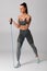 Athletic girl working out with resistance band on gray background. Fitness woman exercises with expander