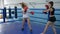 Athletic girls train in short shorts in gym, girl takes blows on boxing paws of strong female in gloved on ring
