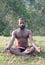 Athletic Indian man meditating in lotus yoga pose in forest