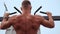 Athletic Man Pumps Up Muscles Doing Pull-Ups Open Sports Ground with Bare Torso